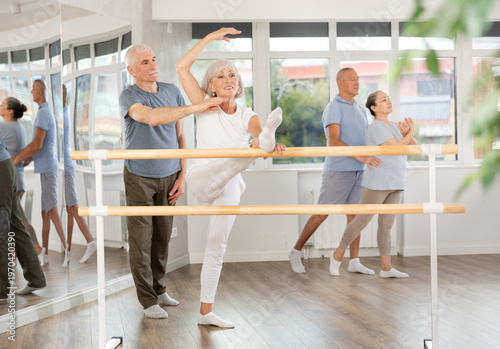 Bilde på lerret Positive old female attendee of ballet courses stretching her leg standing by tr