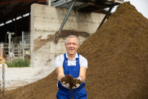 Tableau sur toile During days work in cowshed, senior man employee works with manure, picks up eco