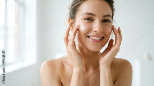 Woman applying face cream smiling brightly in soft light