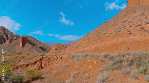 Car navigates dirt road through stunning eroded sandstone mountains in Kyrgyzstan. Pulling back drone view.