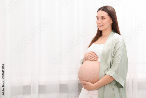 Beautiful pregnant woman touching her belly near curtains at home, space for text Free Download Beautiful pregnant woman touching her belly near curtains at home, space for text - GFXLoad