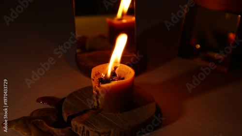 A brightly wind burning candle against a dark background near a mirror, the candle flame dripping melted wax onto the table. A magical witch ritual.