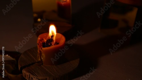A brightly burning candle against a dark background near a mirror, the candle flame dripping melted wax onto the table. A magical witch ritual.