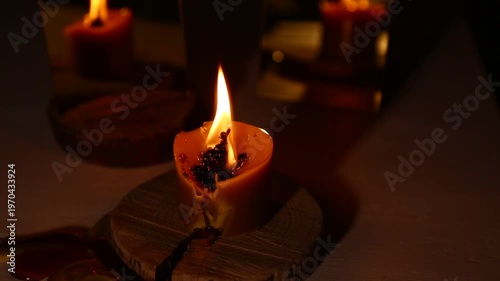 A brightly burning candle against a dark background near a mirror, the candle flame dripping melted wax onto the table. A magical witch ritual.