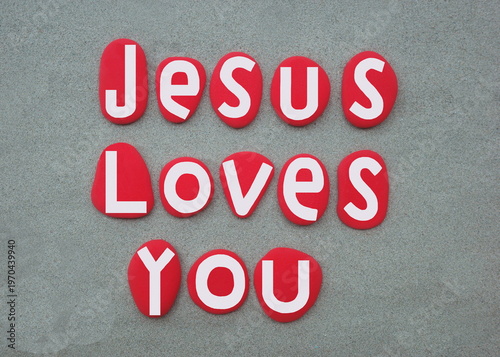 Jesus loves you, message of hope composed with hand painted red colored stone letters over green sand