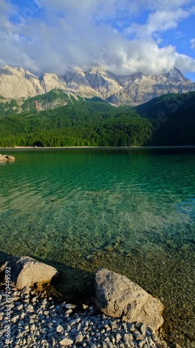 Vertical static video showing the transparent emerald water and rocky shore of Eibsee lake with the Zugspitze range in Germany.