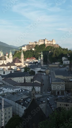 Vertical video of the historic streets of Salzburg, Austria, leading up to the medieval Hohensalzburg Fortress on the hill during the daytime.