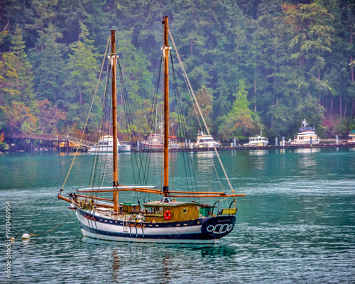 Schilderij op canvas An anchored double-masted sailboat—often called a ketch or schooner—rests calmly on the water, held in place by its anchor line stretching down to the seabed