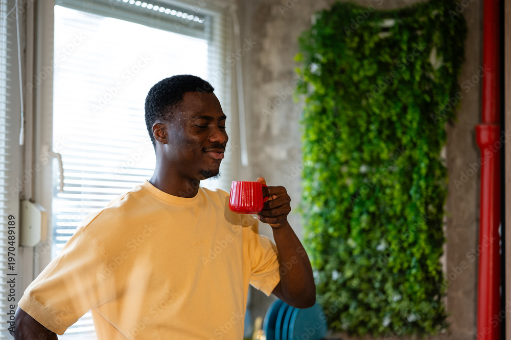 Fototapeta premium Young black man enjoying hot coffee by window