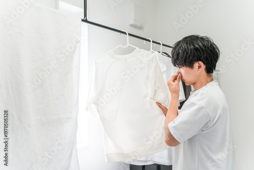 Obraz na plátne A young man is troubled by the smell of his laundry and the musty smell of damp clothes (damp clothes, drying indoors, smell, laundry room)