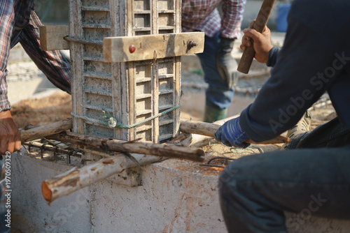 Construction workers assembling wooden supports for a concrete column at a building site.