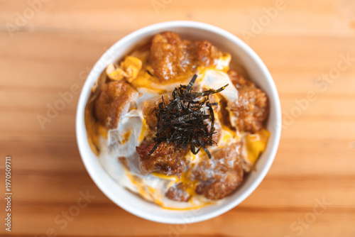 Bowl of crispy fried chicken topped with egg and seaweed on a wooden table.