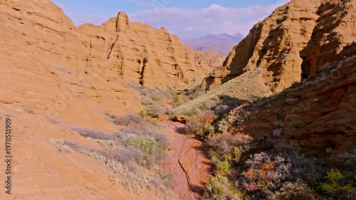 Aerial view captures vast Konorchek canyons in Kyrgyzstan, showcasing eroded sandstone formations and dry riverbed. Sparse vegetation adds to serene landscape.