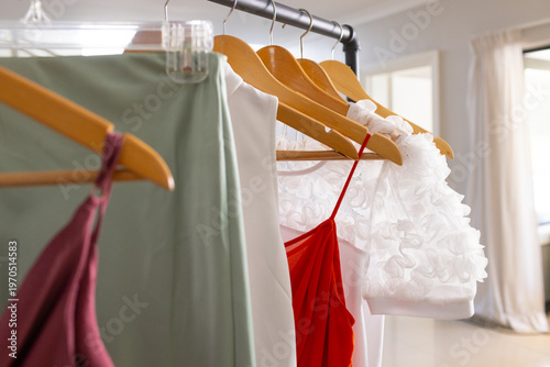 Sunlight streaming through window, garments on wooden hangers catching light for fashion display