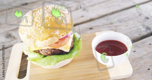 Displaying sesame burger resting on wood board with cheese, ketchup bowl and AR icons, copy space