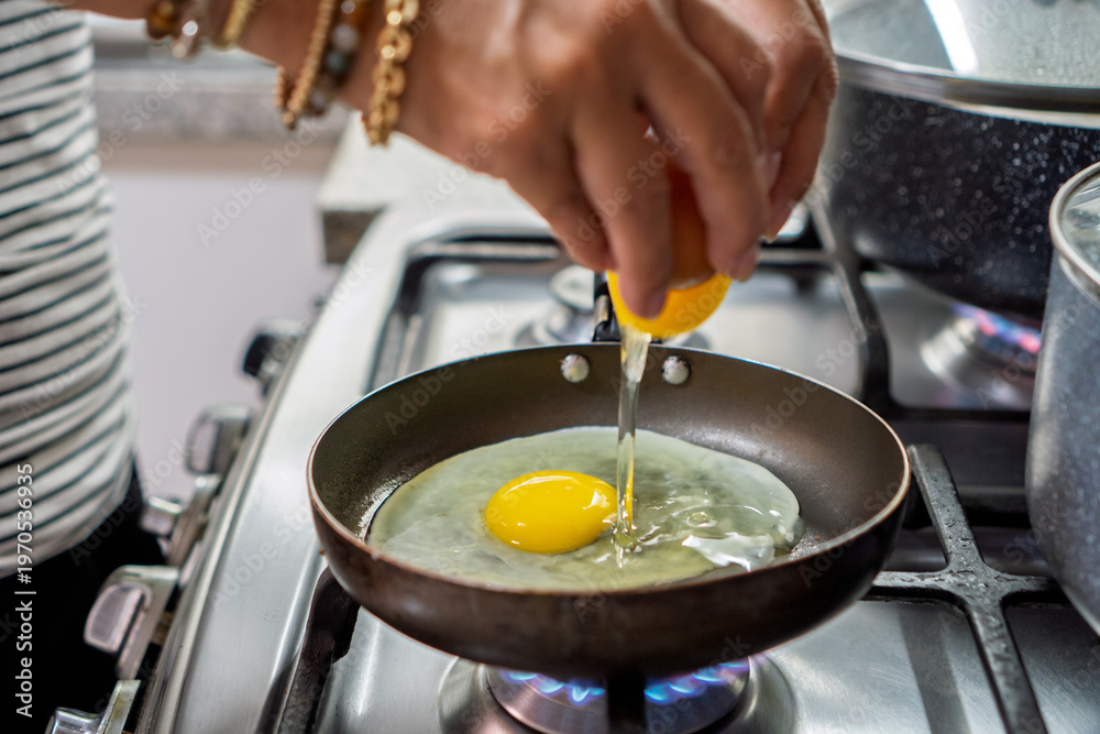 Fototapeta premium Hands cracking fresh egg into frying pan for breakfast