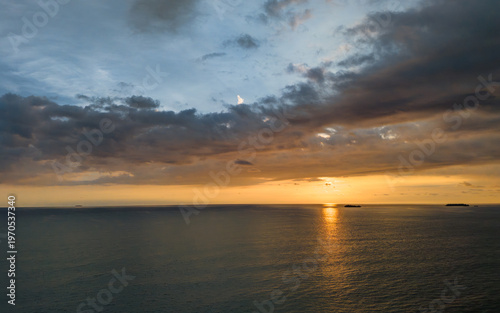 Golden sunlight dances on calm ocean waves at sunset over distant islands