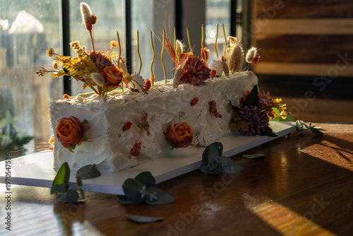 Rectangular white frosted cake elegantly decorated with dried autumn-toned flowers.