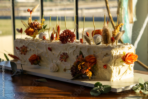 Rectangular white frosted cake elegantly decorated with dried autumn-toned flowers.