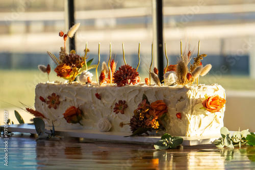 Rectangular white frosted cake elegantly decorated with dried autumn-toned flowers.