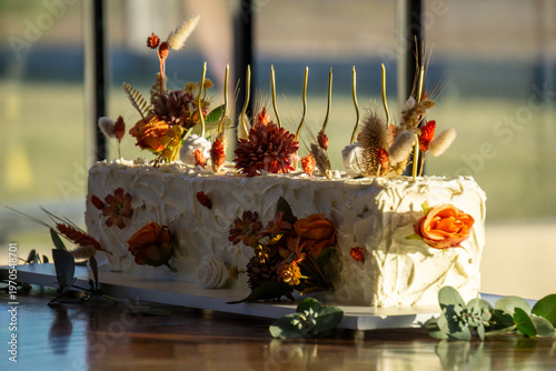 Rectangular white frosted cake elegantly decorated with dried autumn-toned flowers.