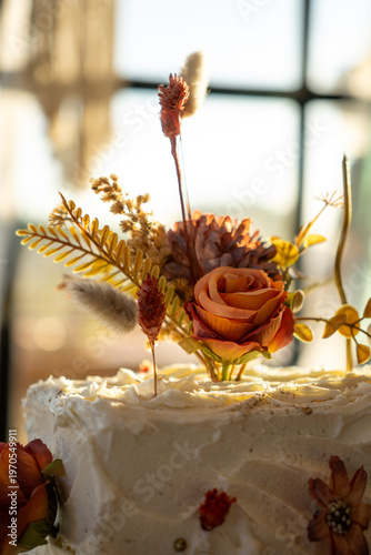 Rectangular white frosted cake elegantly decorated with dried autumn-toned flowers.