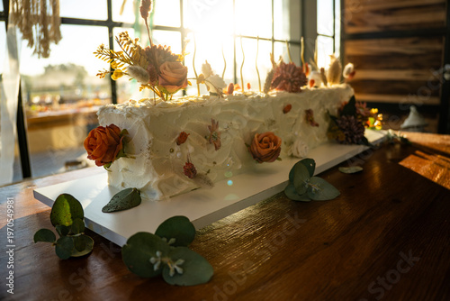 Rectangular white frosted cake elegantly decorated with dried autumn-toned flowers.