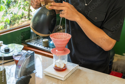 Foto Barista hand pouring V60 pour over coffee with kettle into dripper over ice on scale, Japanese iced coffee flash brew method in natural light kitchen