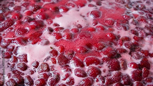 Whole and halved strawberries submerged in frothy pink liquid create a warm, inviting atmosphere. Scene evokes feelings of deliciousness and home cooking.