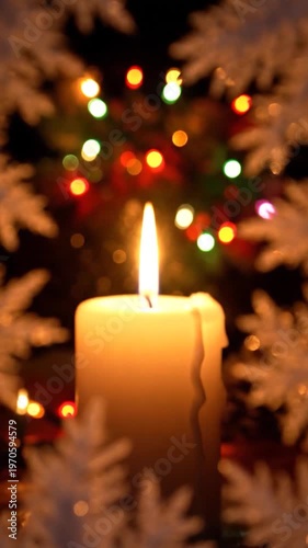 A single lit candle glows warmly through frosted branches, with colorful blurred festive lights in the background