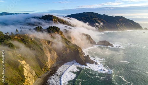 Coastal cliffs shrouded in fog, meeting ocean waves under a partly cloudy sky
