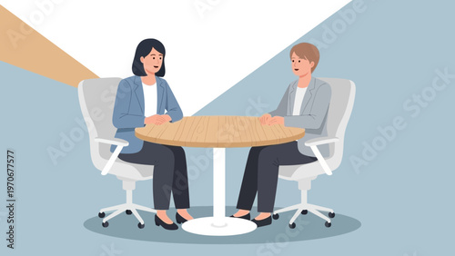 Two women in business attire discussing at a round table in a modern office.