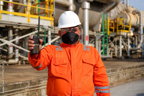 Photos Industrial worker in hard hat and mask holding walkie-talkie at refinery