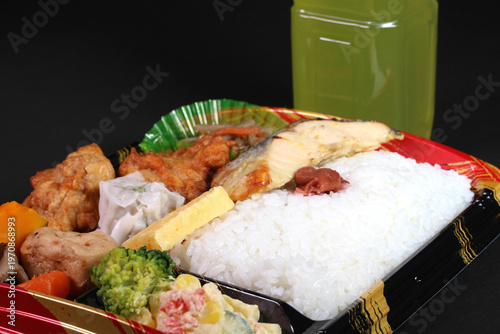 黒背景に置かれたパック入りの弁当とペットボトルのお茶