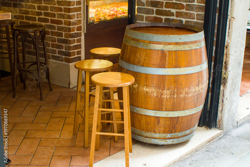 Weathered wooden barrels serve as tables for patrons to rest their drinks. Sturdy timber stools stand ready on the terracotta tiles, inviting passersby to pause and soak in the rustic aesthetic.