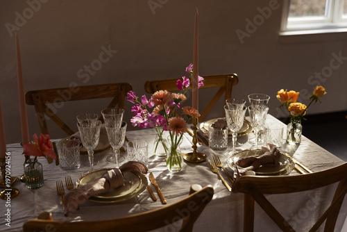 Slika na platnu Elegant tablescape with golden cutlery, crystal glasses, and pink flowers on a linen cloth