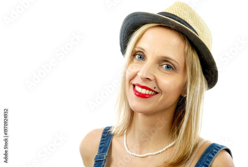 Young woman smiling, wearing straw hat and denim overalls. Red lipstick and pearl necklace visible. Hair blonde, eyes blue. Clean white background. Studio shot, isolated subject