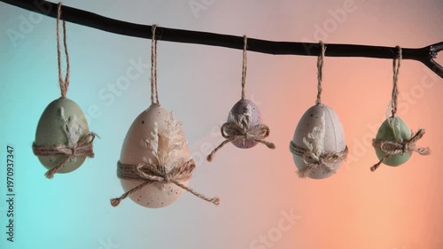 Pastel easter eggs in green, white, and purple hang from a natural branch, tied with twine bows and dried leaves against a vibrant background for spring celebration