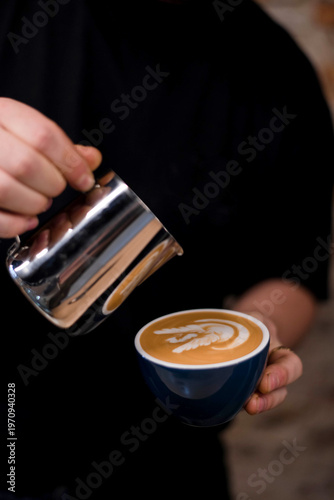 Barista pouring milk into a coffee mug, close-up of a barista's hand pouring milk for making latte swan art in a cafe.