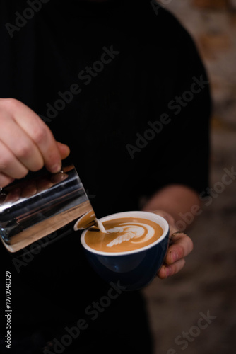 A skilled barista carefully pours steamed milk into a cup of espresso, creating an intricate latte art design.