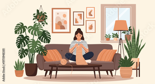 Young woman sitting comfortably on a brown sofa and knitting a long scarf in a cozy living room filled with many green plants.
