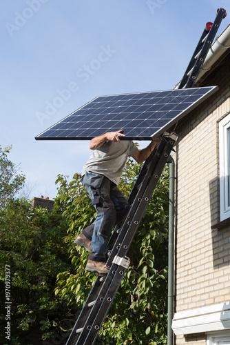 Man carrying a solar panel to a roof using a ladder in the Netherlands