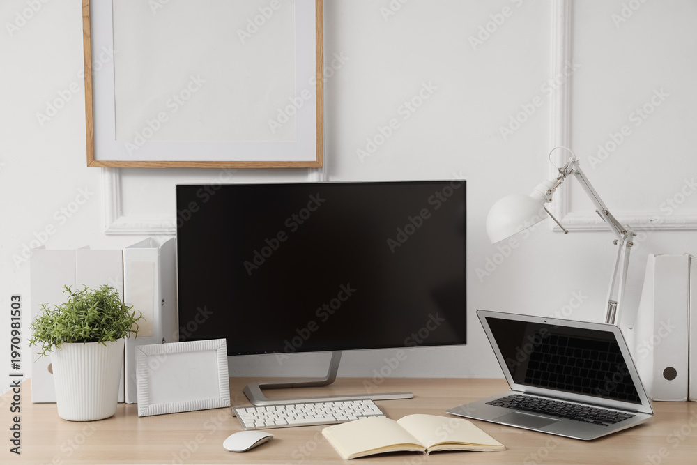 Fototapeta premium Workplace with blank computer monitor, laptop and lamp near light wall in office