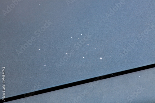 A vehicle surface shows multiple small white spots, indicating issues with the car paint. This is visible in daylight on a clear surface.
