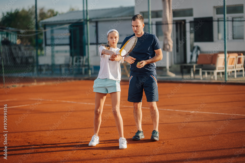 Obraz premium Tennis coach teaching girl forehand on clay court