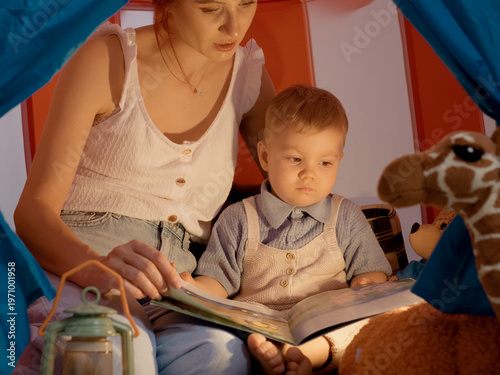 Cuadro en lienzo A mother reads a colorful storybook to her young son in a cozy tent