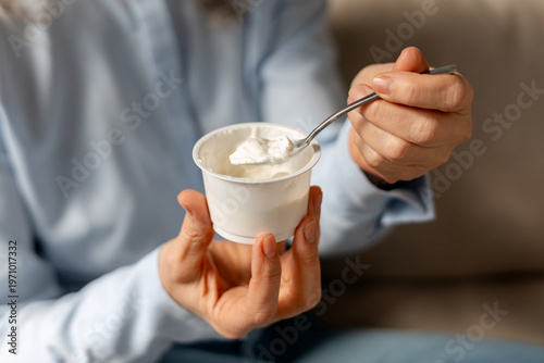 Canvas Print Hands holding an open yogurt cup, eating a spoonful of dairy product