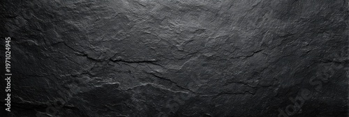 A panoramic view of a textured black slate stone surface with natural cracks and ridges. The matte finish and dramatic lighting create a dark and moody background for design.