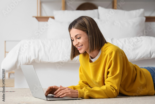 Beautiful woman using laptop to search online on carpet in bedroom