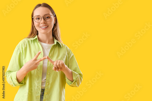 Young woman using sign language on yellow background